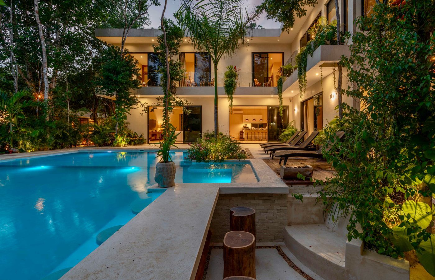 Modern tropical villa and illuminated swimming pool at dusk.